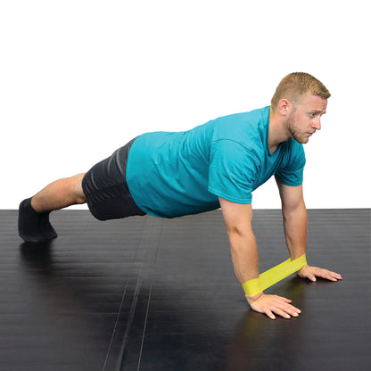 A man performs a plank using a CanDo Band Exercise Loop around his wrists on a black mat.