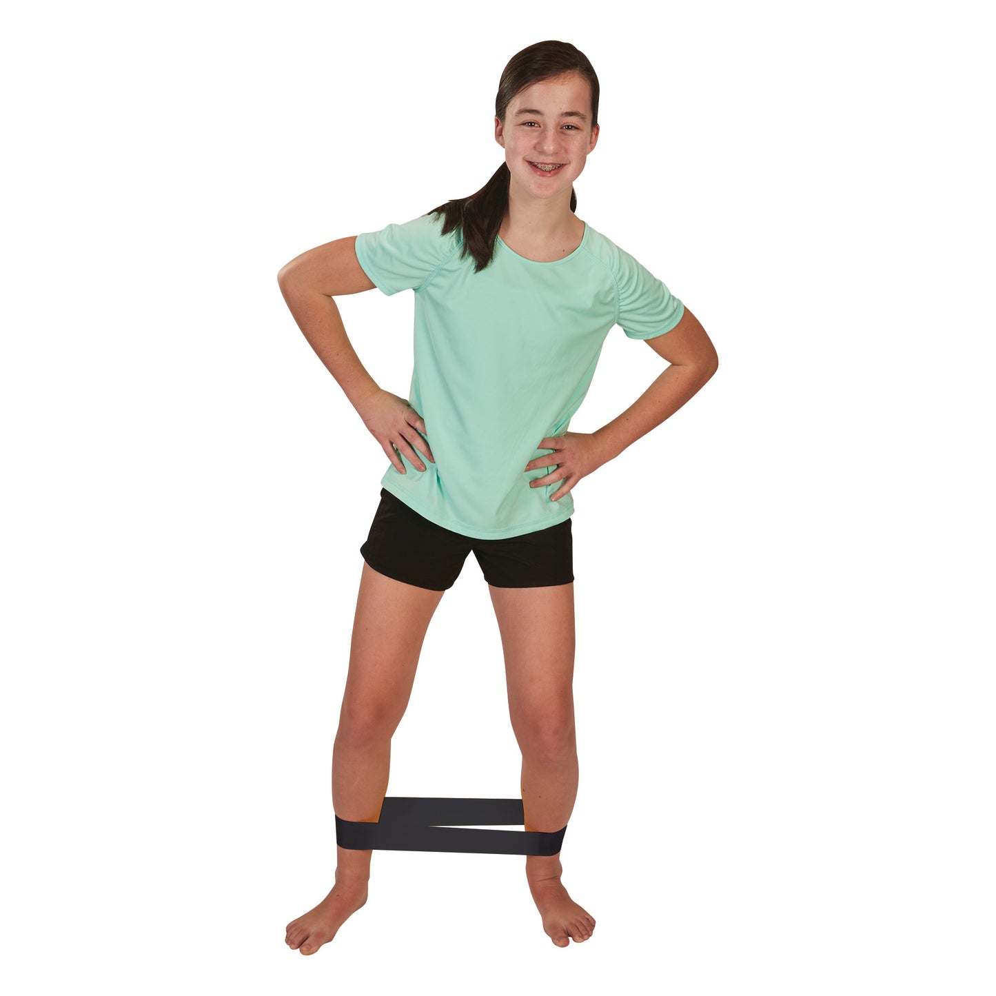 A girl in a mint T-shirt and black shorts exercises with a CanDo Band Exercise Loop around her ankles, standing with hands on hips.