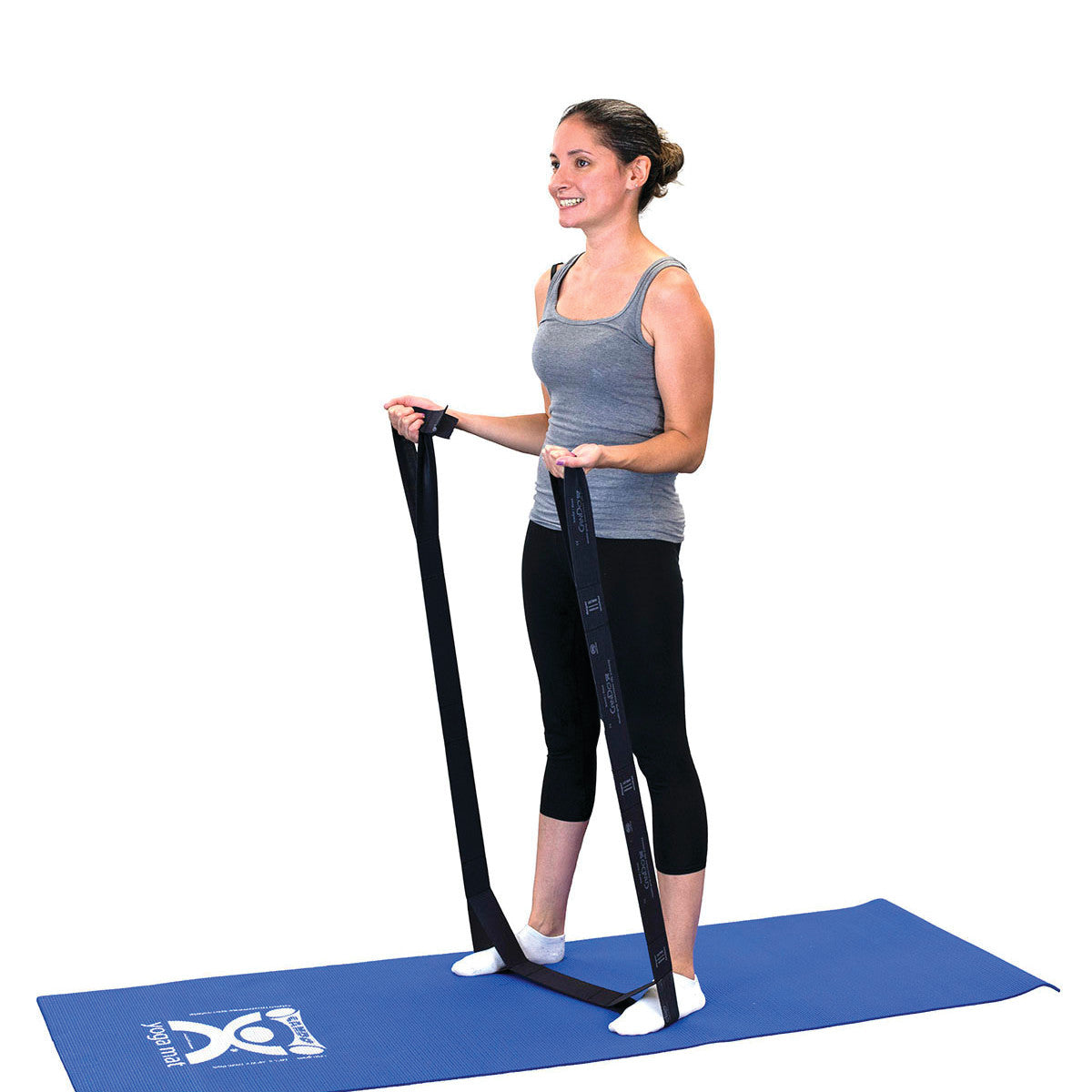 A person stands on a blue mat using the CanDo Multi-Grip Exerciser, gripping it with both hands for resistance training.
