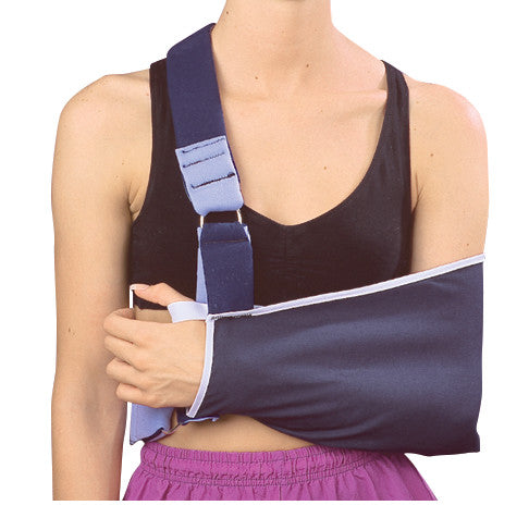 A person wears a Shoulder Immobilizer with Body Strap, holding their left arm in a sling, with a black top and purple shorts.