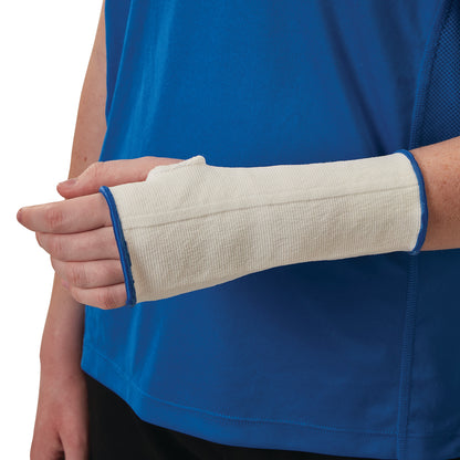 A person wearing an AliMed Wrist Compression Sleeve in white, with blue trim, over their lower arm and wrist, is standing against a blue shirt.