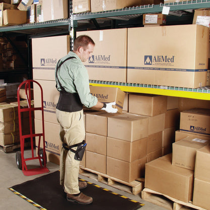 A person wearing an AliMed SoftEdge Edge Protector lifts a box in a warehouse with stacked AliMed boxes and a red dolly nearby.