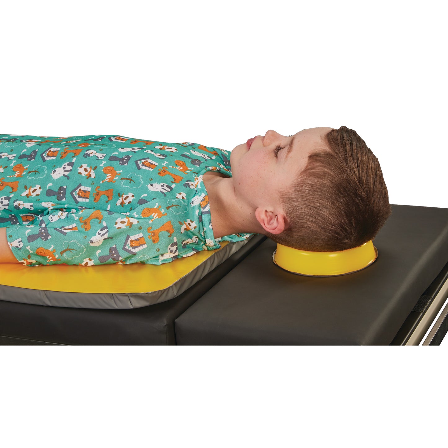 A child is lying on a medical table using the AliMed AliLite Head Donut for head support, wearing a printed hospital gown.