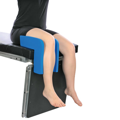 A person sits on a table using the AliMed Vinyl-Coated Well-Leg Holder to support the knees, with legs hanging down.