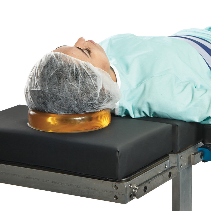A person lies on a medical table using the AliMed AliGel Head Donut, a supportive gel cushion for the head in surgical settings.