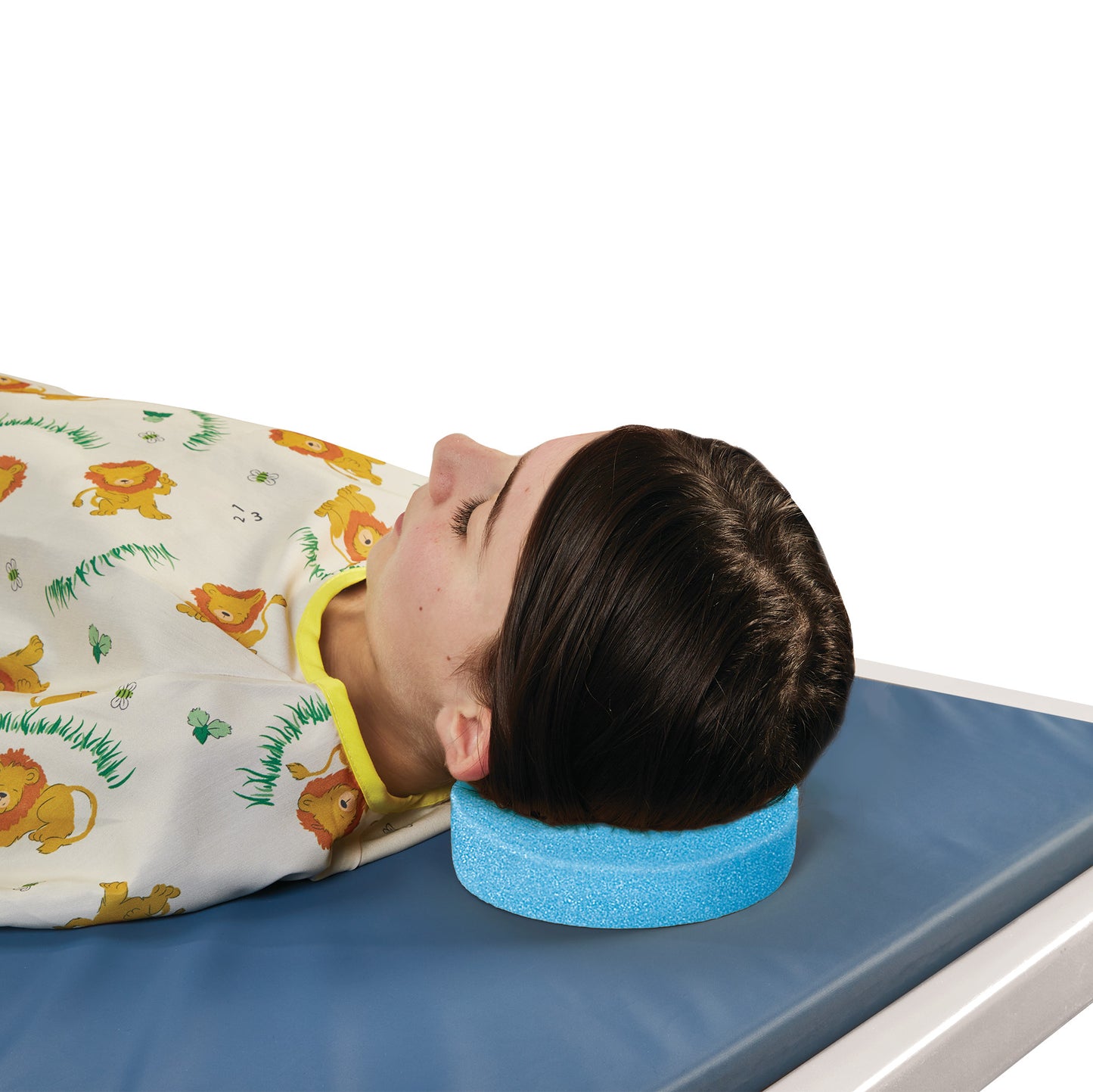 A patient rests their head on an AliMed Disposable Foam Head Donut while lying on a blue mat, covered with a lion-patterned gown.