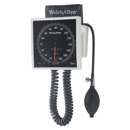 The Welch Allyn 767 Tycos Aneroid sphygmomanometer with a black dial, flexible tubing, and inflation bulb is shown mounted on a wall.