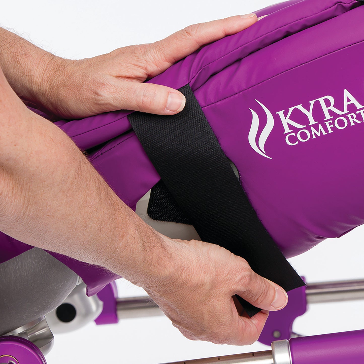 Hands are adjusting the KYRA Comfort 350 Lithotomy Stirrup with Hook-and-Loop Straps, featuring a purple cushioned surface.
