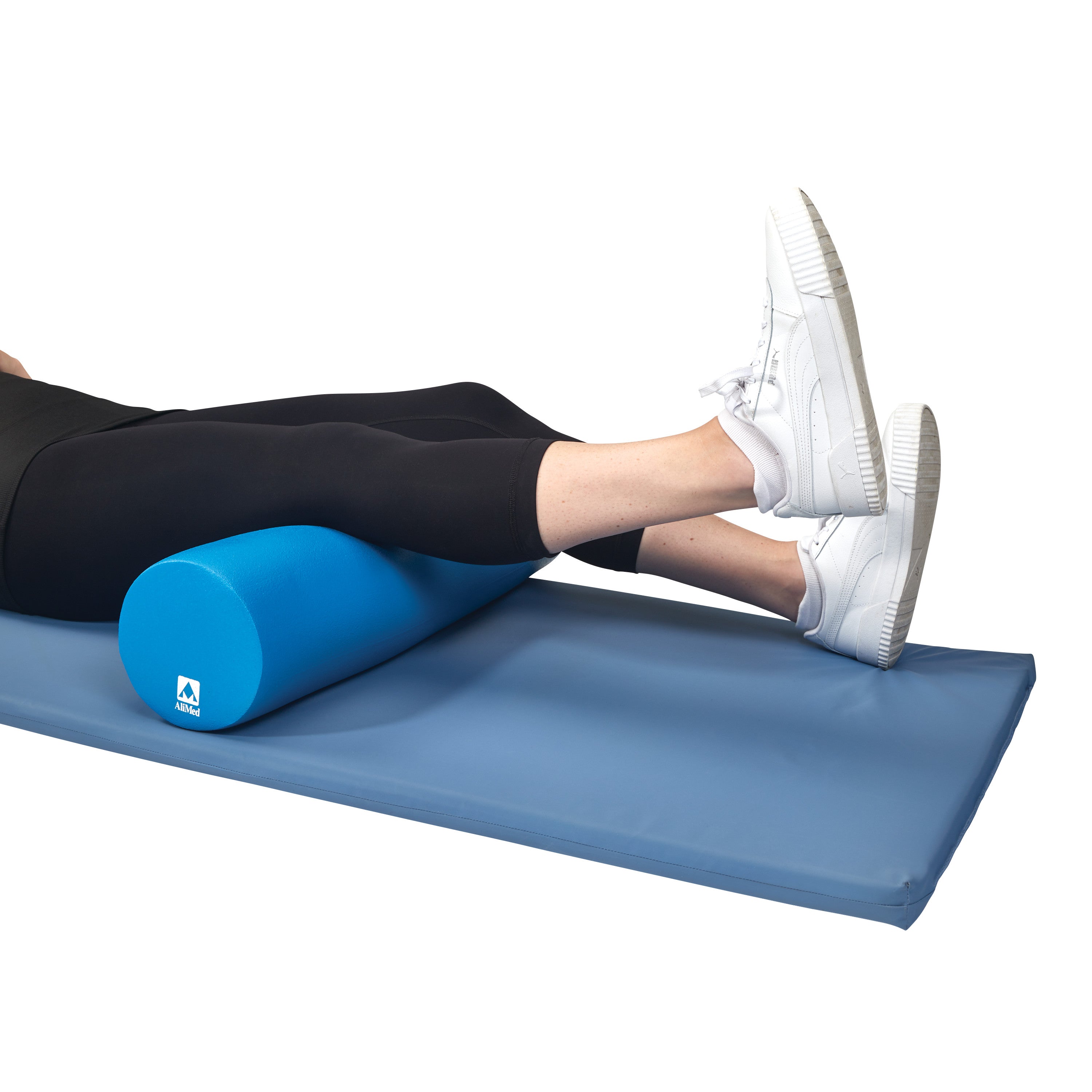 A person lies on a mat with legs elevated on a blue AliMed Antimicrobial-Treated Therapy Positioning Wedge, wearing white sneakers.