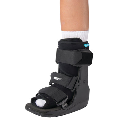 A person wears the Ossur Formfit Low-Top Walker on their left foot. It is black with adjustable straps and an open-toe design.