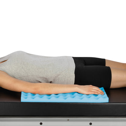 A person lies on a table using an AliMed Single-Use Foam Ulnar Pad/Toboggan Liner, a blue wavy foam pad supporting the arm.