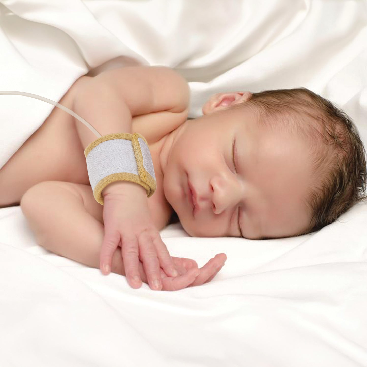 A newborn sleeps on a white blanket with an AliMed AliStrap Soft Positioning Strap around their arm.