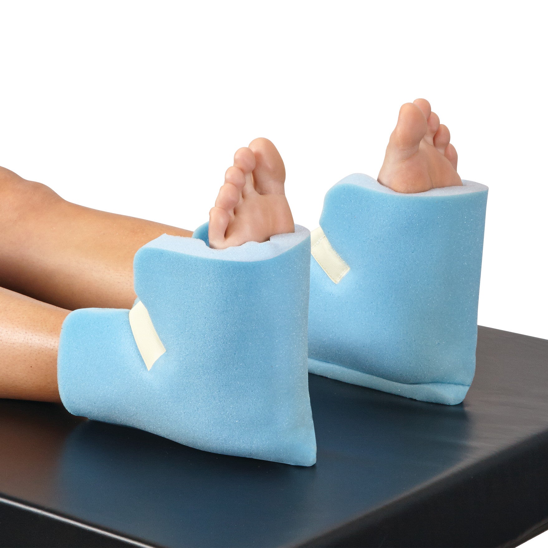 Feet are resting on AliMed Disposable Foam Heel Pads, which are blue with white straps, placed on a dark surface.