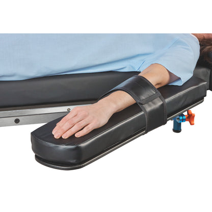 A person's arm is secured on a padded platform with the AliMed Reusable Armboard Strap. The armboard is attached to a surface.